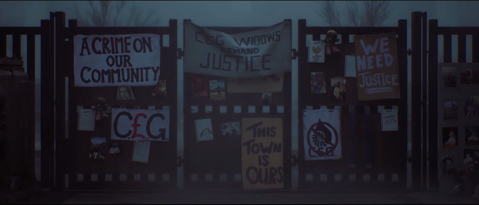 A gate covered in banners and photographs of the victims in Silent Hill: Townfall